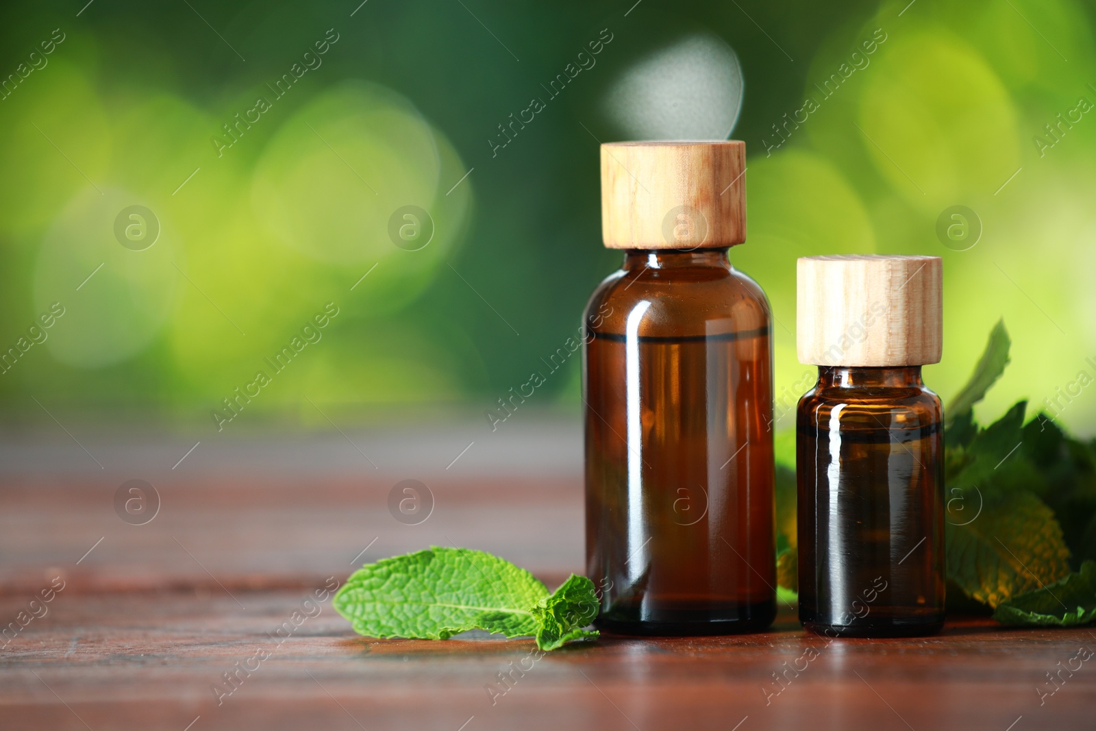 Photo of Bottles of mint essential oil and fresh leaves on wooden table, space for text