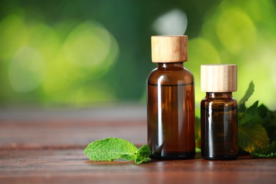 Bottles of mint essential oil and fresh leaves on wooden table, space for text