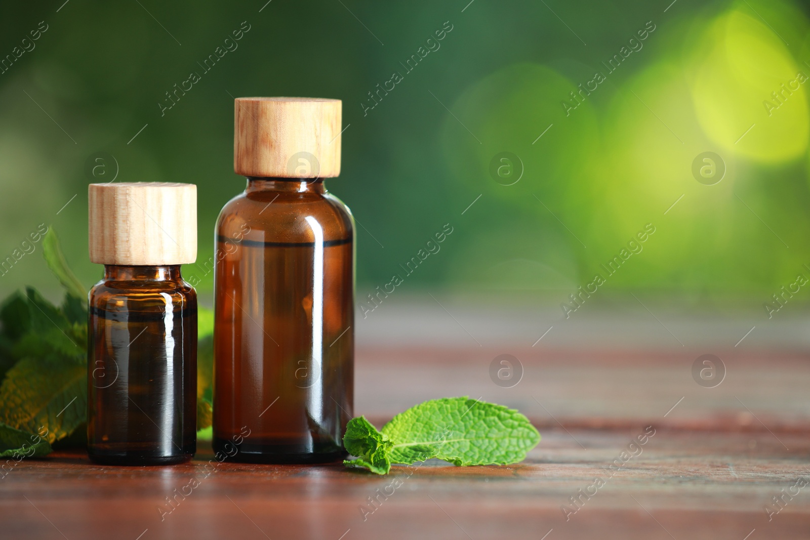 Photo of Bottles of mint essential oil and fresh leaves on wooden table, space for text