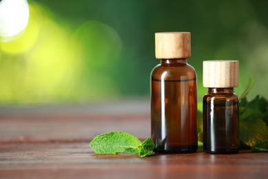 Photo of Bottles of mint essential oil and fresh leaves on wooden table, space for text