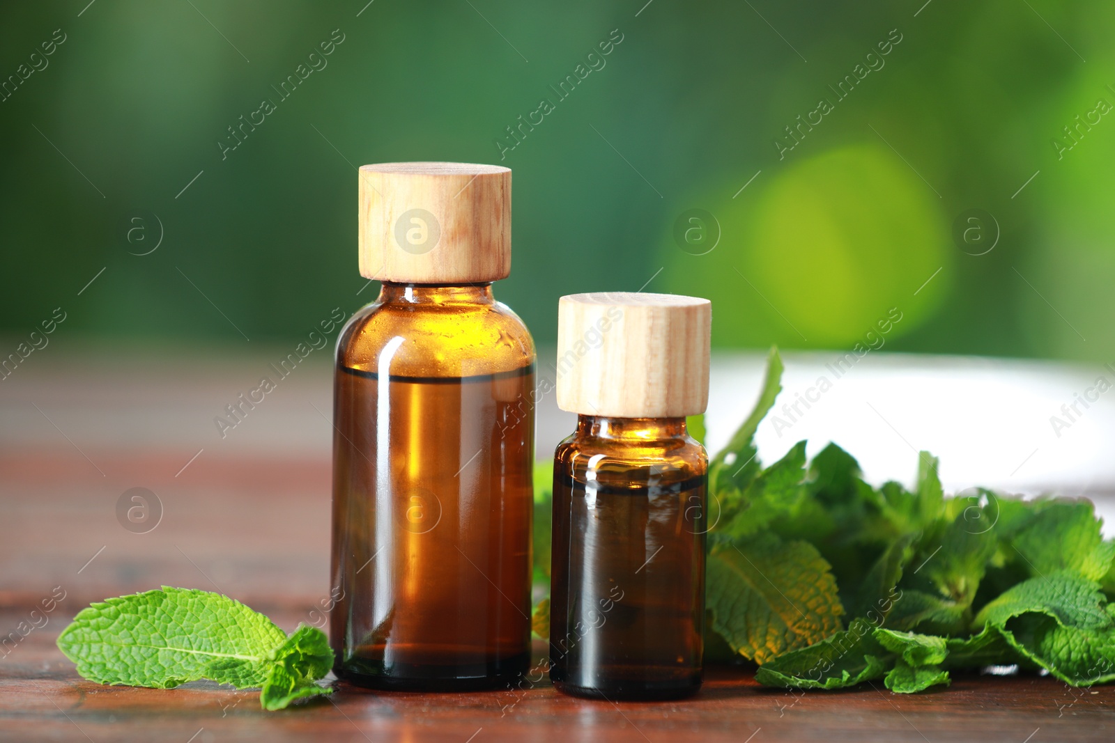 Photo of Bottles of mint essential oil and fresh leaves on wooden table