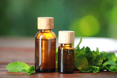 Bottles of mint essential oil and fresh leaves on wooden table