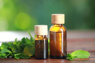 Bottles of mint essential oil and fresh leaves on wooden table