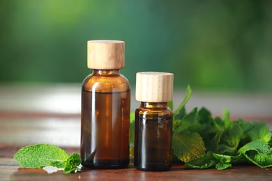 Bottles of mint essential oil and fresh leaves on wooden table