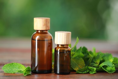 Bottles of mint essential oil and fresh leaves on wooden table