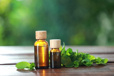 Photo of Bottles of mint essential oil and fresh leaves on wooden table