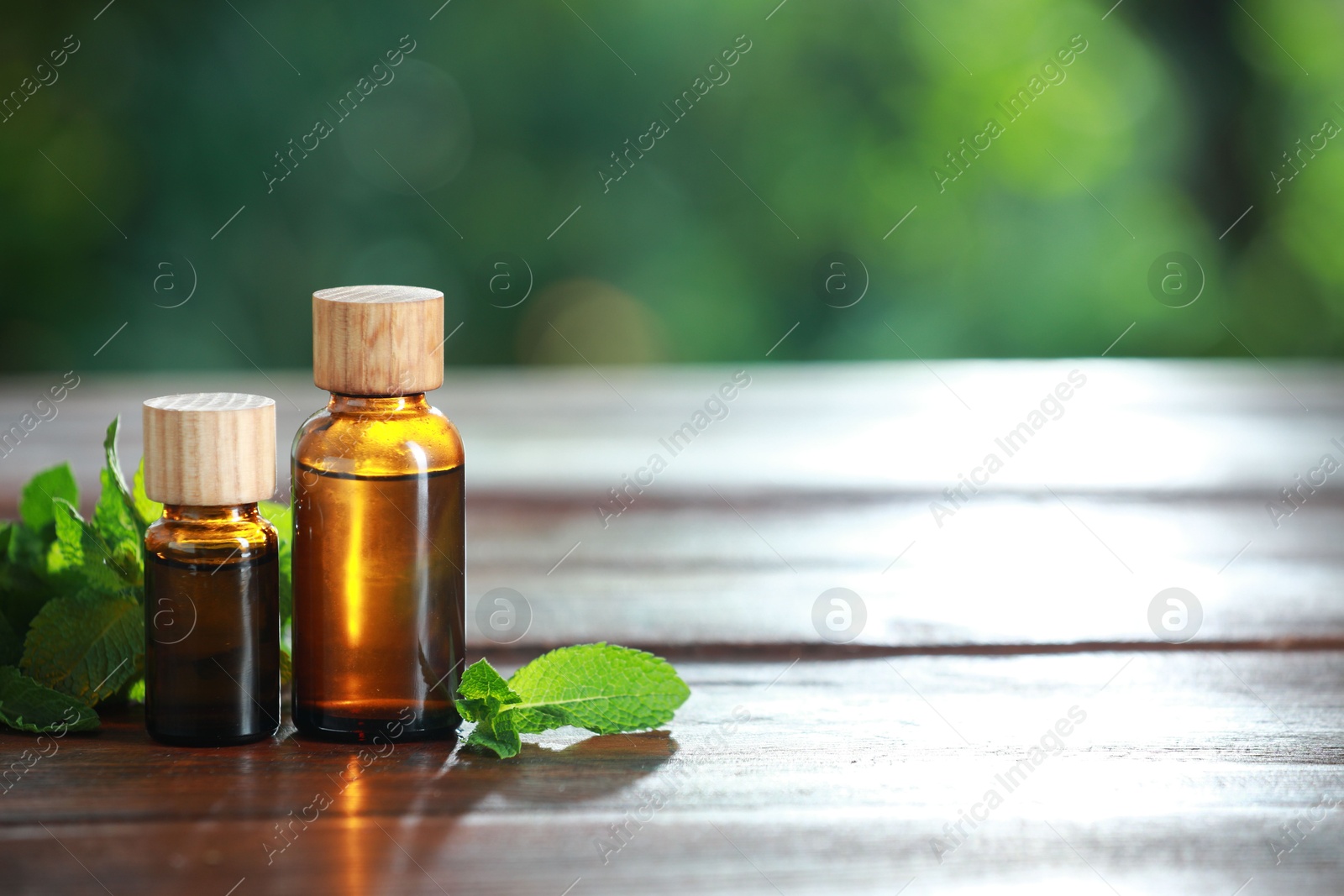 Photo of Bottles of mint essential oil and fresh leaves on wooden table, space for text