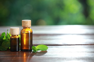 Bottles of mint essential oil and fresh leaves on wooden table, space for text