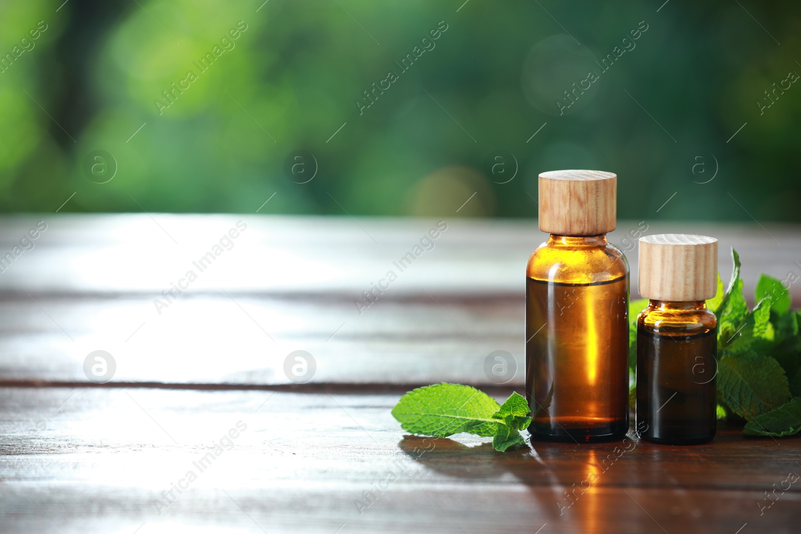 Photo of Bottles of mint essential oil and fresh leaves on wooden table, space for text