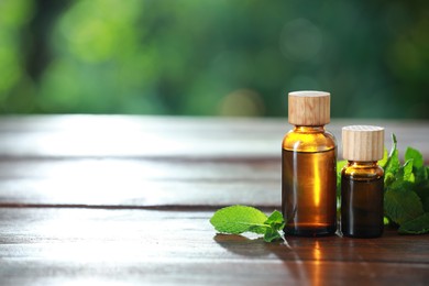 Bottles of mint essential oil and fresh leaves on wooden table, space for text