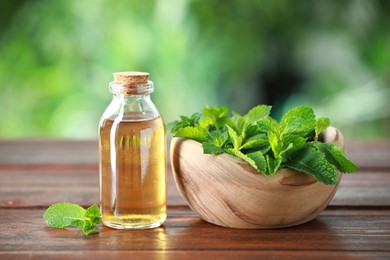 Bottle of mint essential oil and fresh leaves on wooden table