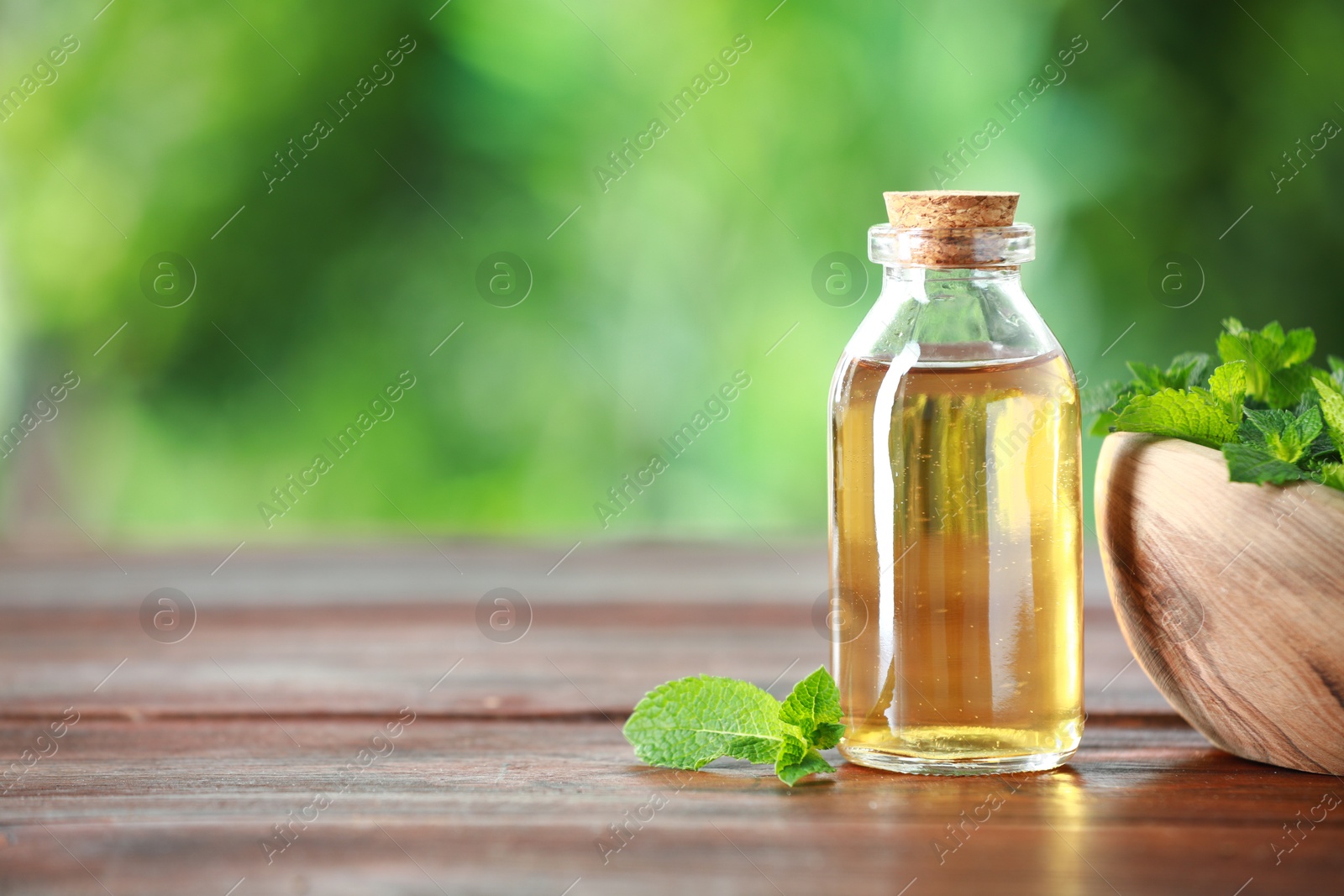 Photo of Bottle of mint essential oil and fresh leaves on wooden table, space for text