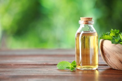 Bottle of mint essential oil and fresh leaves on wooden table, space for text