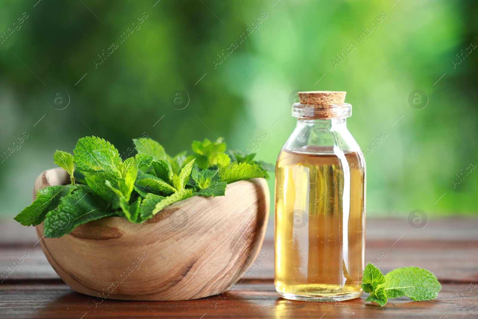 Photo of Bottle of mint essential oil and fresh leaves on wooden table