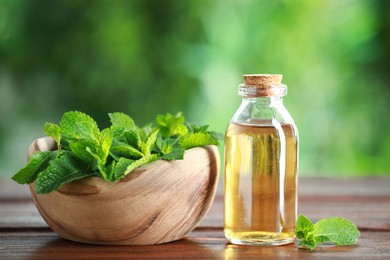 Bottle of mint essential oil and fresh leaves on wooden table