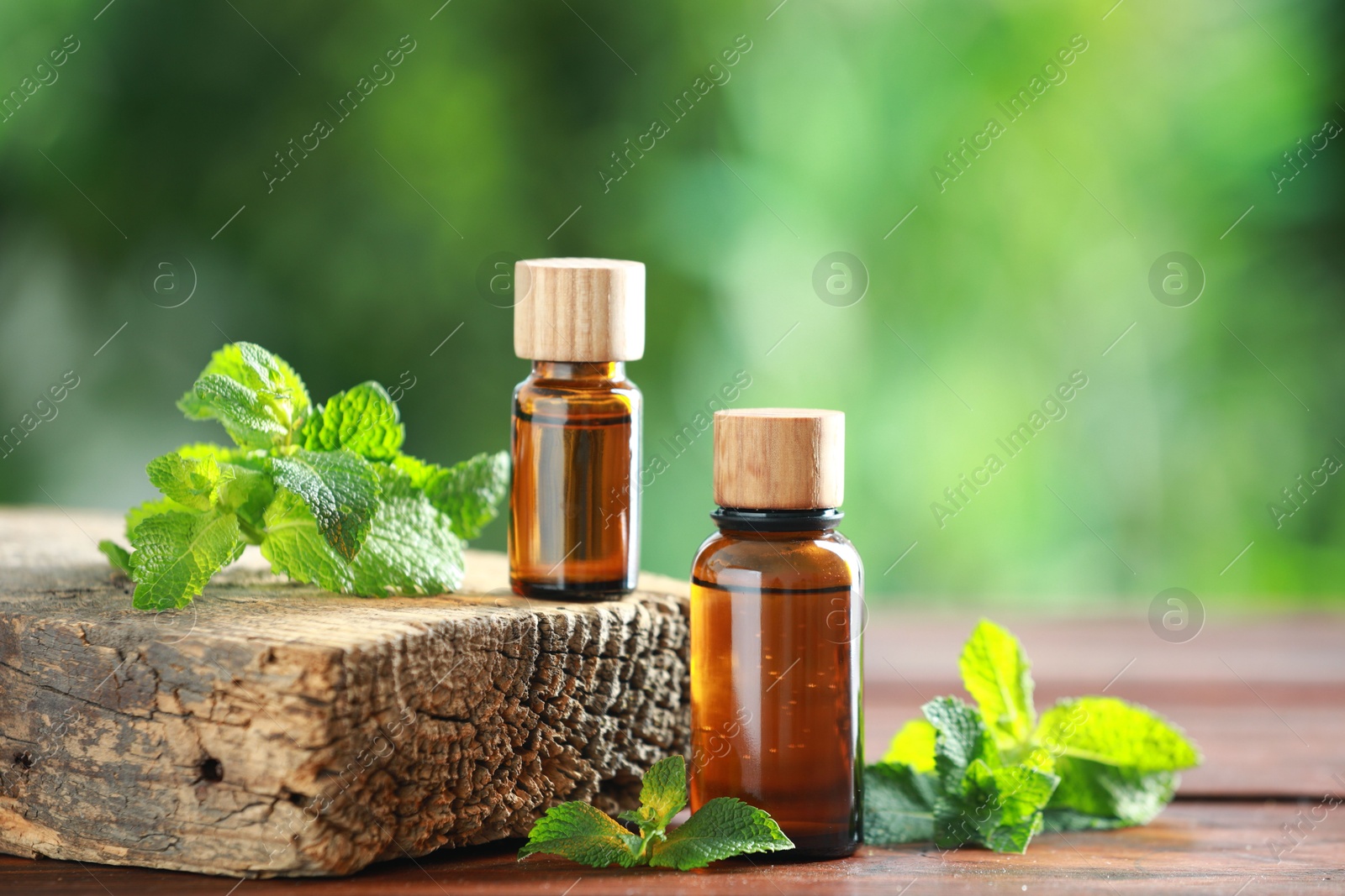 Photo of Bottles of mint essential oil and fresh leaves on wooden table