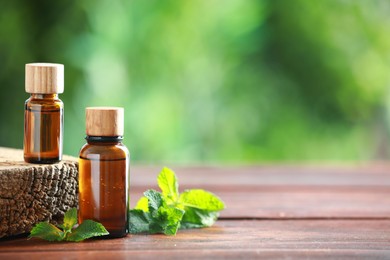 Bottles of mint essential oil and fresh leaves on wooden table, space for text