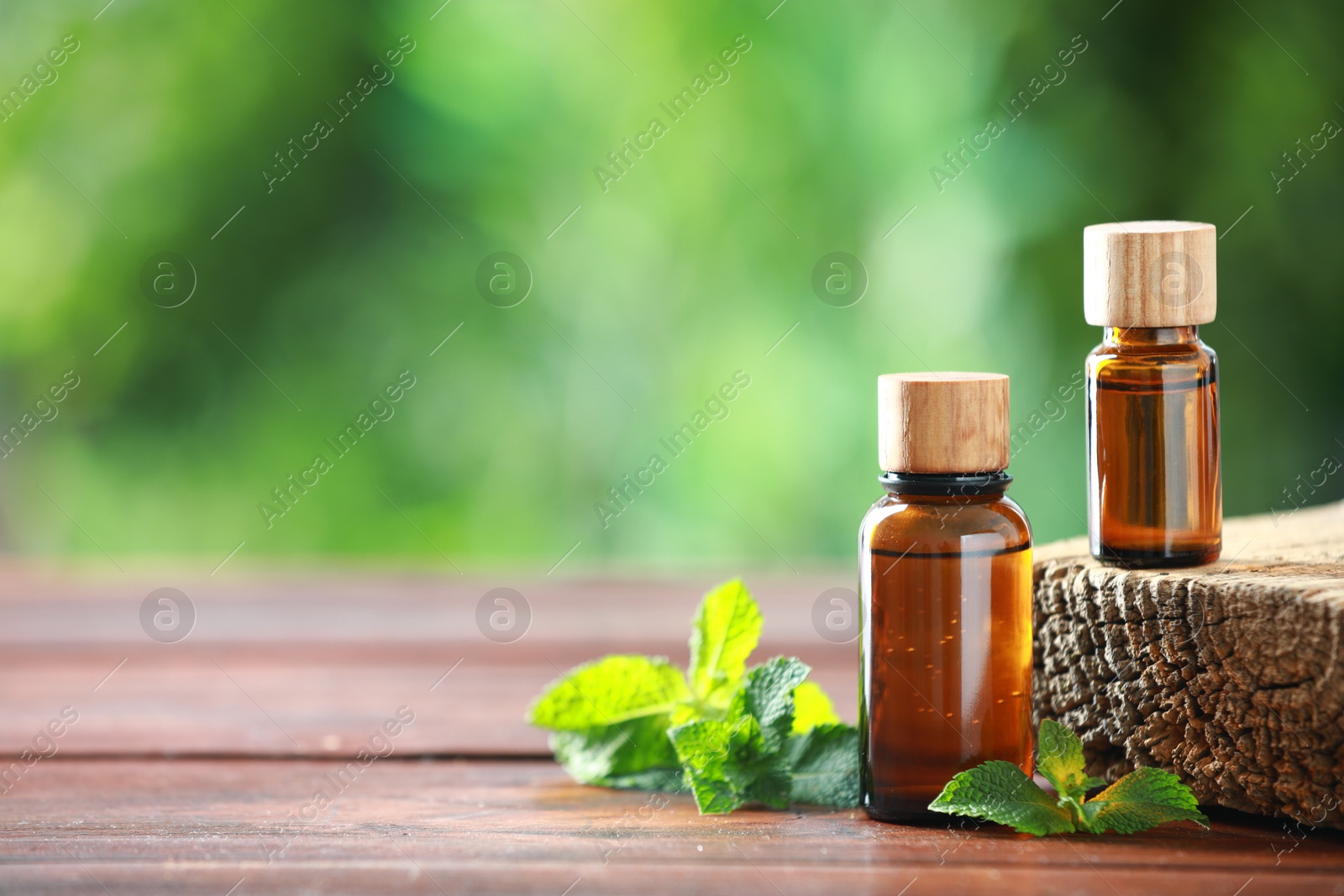 Photo of Bottles of mint essential oil and fresh leaves on wooden table, space for text