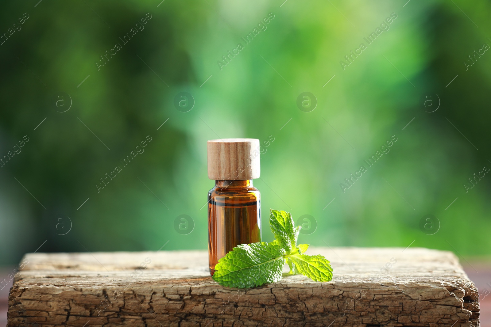 Photo of Bottle of mint essential oil and fresh leaves on wooden table