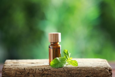 Bottle of mint essential oil and fresh leaves on wooden table