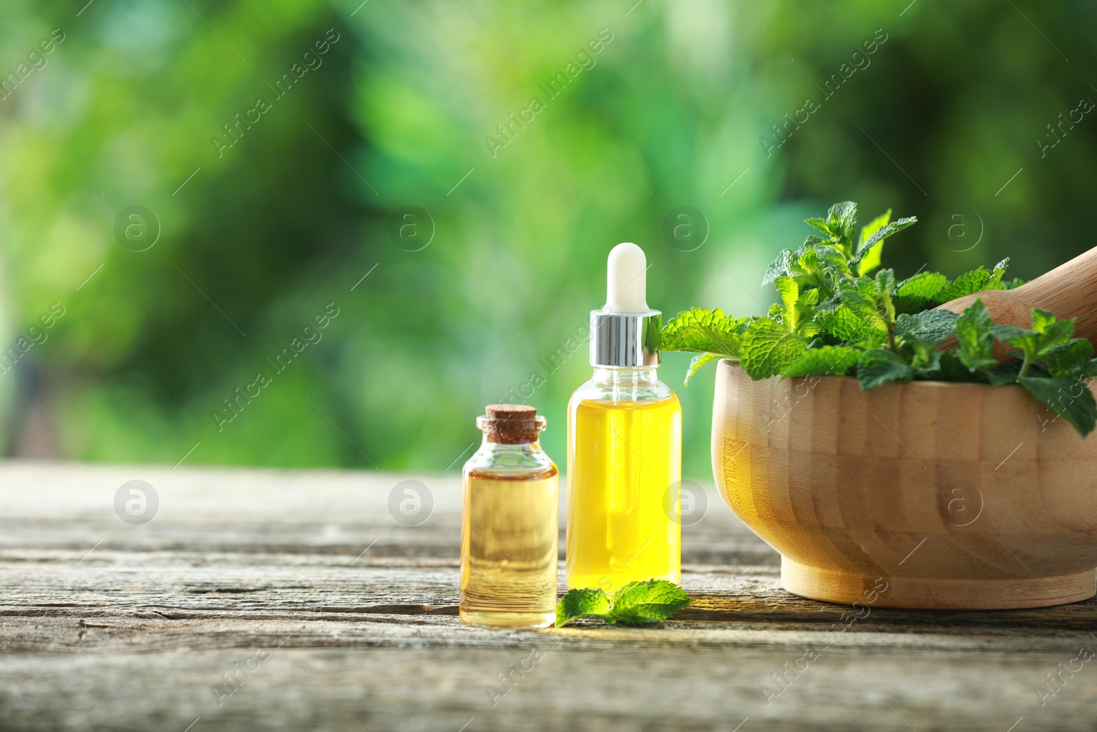 Photo of Bottles of mint essential oil and fresh leaves on wooden table, space for text