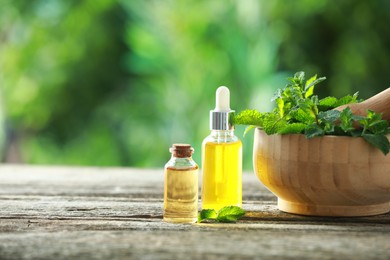 Bottles of mint essential oil and fresh leaves on wooden table, space for text