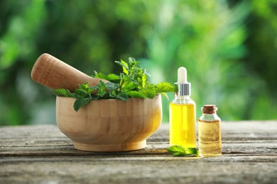 Bottles of mint essential oil and fresh leaves on wooden table