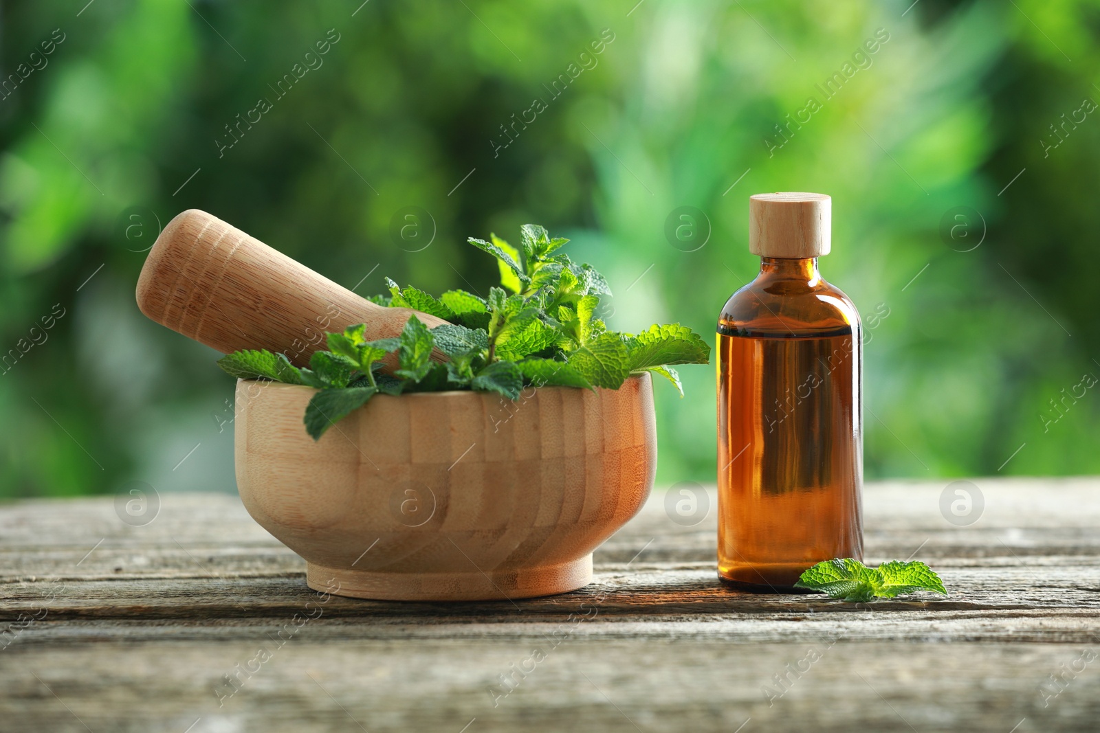 Photo of Bottle of mint essential oil and fresh leaves on wooden table