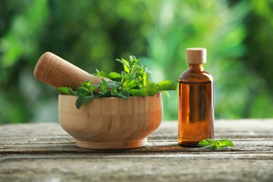 Photo of Bottle of mint essential oil and fresh leaves on wooden table