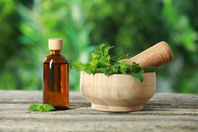 Bottle of mint essential oil and fresh leaves on wooden table