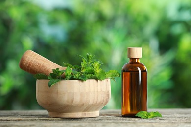 Bottle of mint essential oil and fresh leaves on wooden table