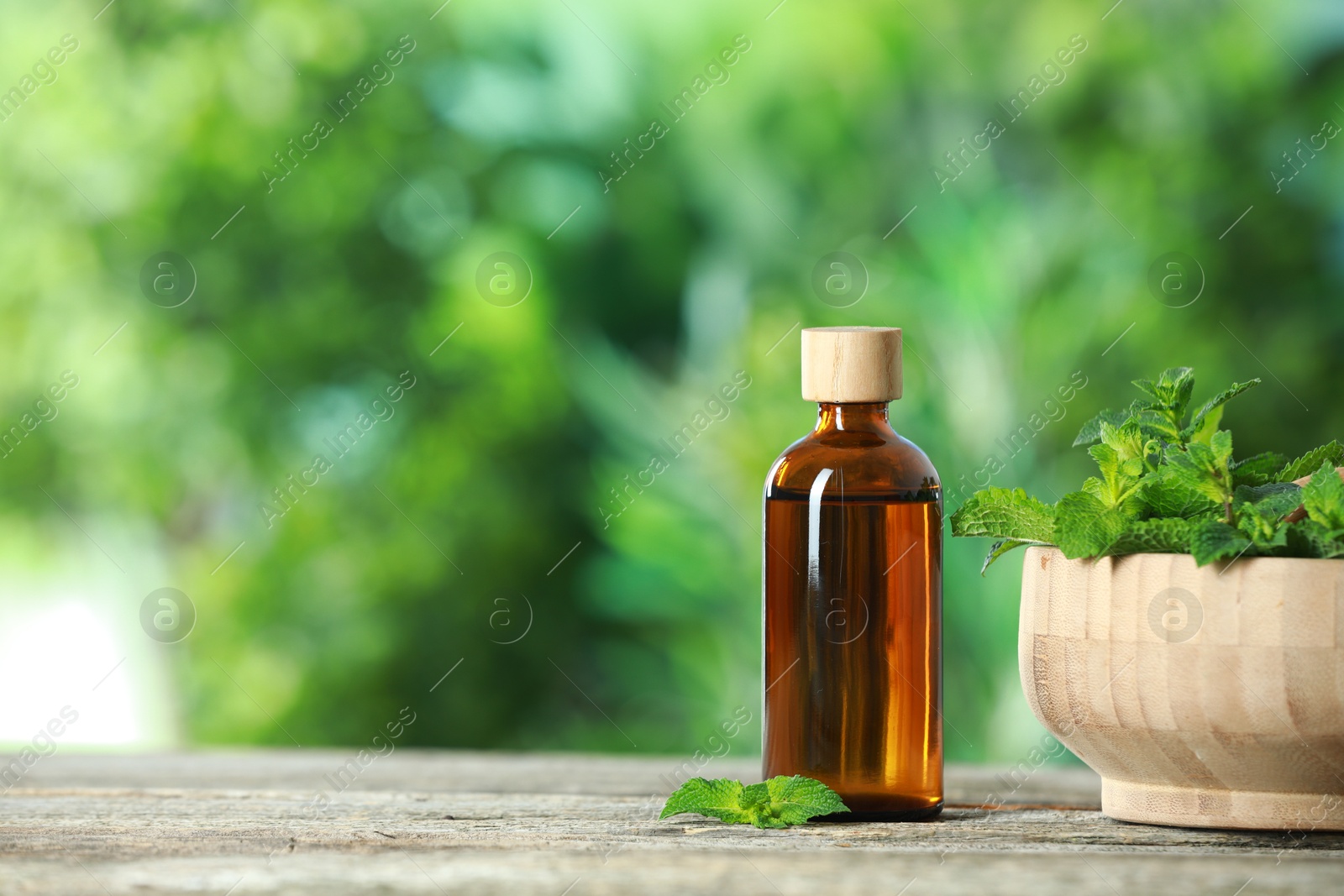 Photo of Bottle of mint essential oil and fresh leaves on wooden table, space for text