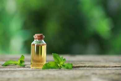 Photo of Bottle of mint essential oil and fresh leaves on wooden table, space for text