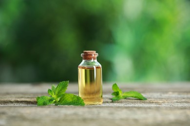 Bottle of mint essential oil and fresh leaves on wooden table