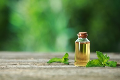 Photo of Bottle of mint essential oil and fresh leaves on wooden table, space for text