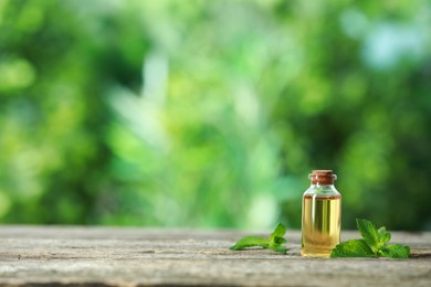 Photo of Bottle of mint essential oil and fresh leaves on wooden table, space for text