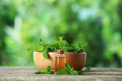 Photo of Bottle of mint essential oil and fresh leaves on wooden table