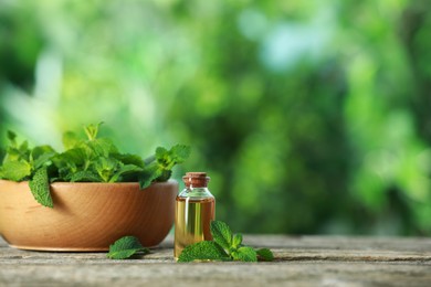 Bottle of mint essential oil and fresh leaves on wooden table, space for text