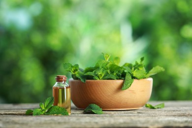 Bottle of mint essential oil and fresh leaves on wooden table