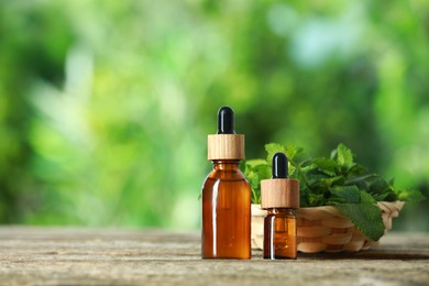 Photo of Bottles of mint essential oil and fresh leaves on wooden table, space for text