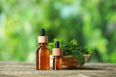 Photo of Bottles of mint essential oil and fresh leaves on wooden table