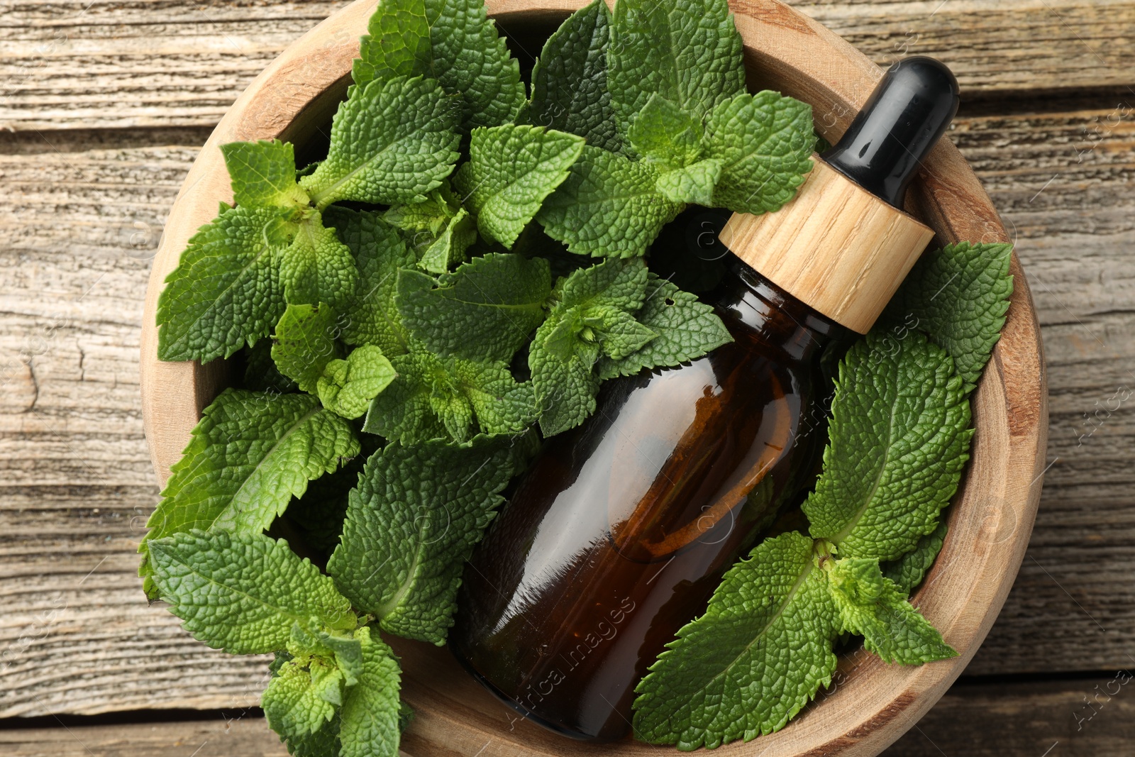 Photo of Bottle of mint essential oil and fresh leaves on wooden table, top view