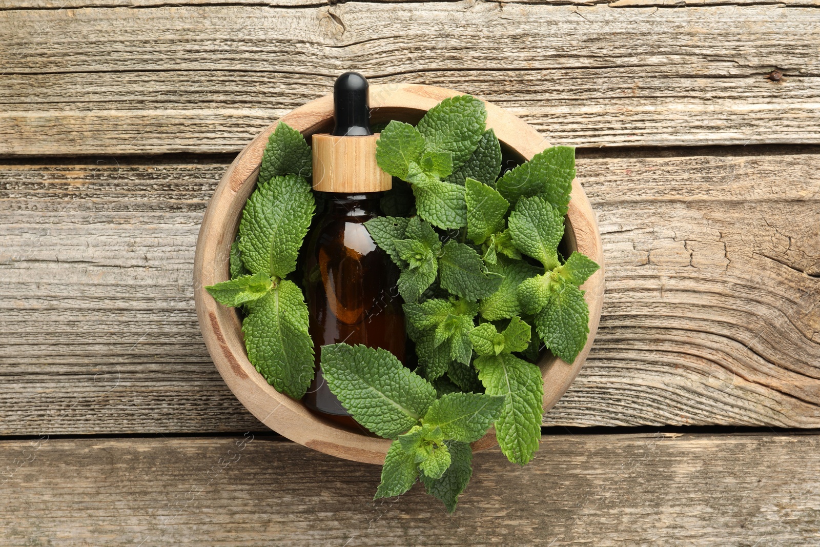 Photo of Bottle of mint essential oil and fresh leaves on wooden table, top view