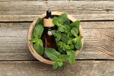 Bottle of mint essential oil and fresh leaves on wooden table, top view