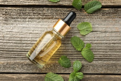 Photo of Bottle of mint essential oil and fresh leaves on wooden table, top view