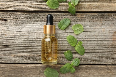 Photo of Bottle of mint essential oil and fresh leaves on wooden table, top view