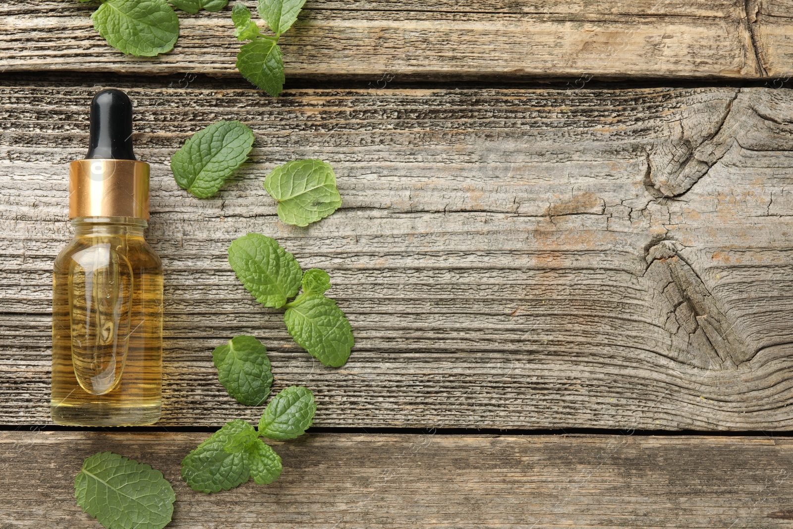 Photo of Bottle of mint essential oil and fresh leaves on wooden table, top view. Space for text