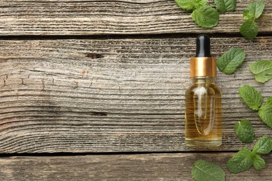 Photo of Bottle of mint essential oil and fresh leaves on wooden table, top view. Space for text