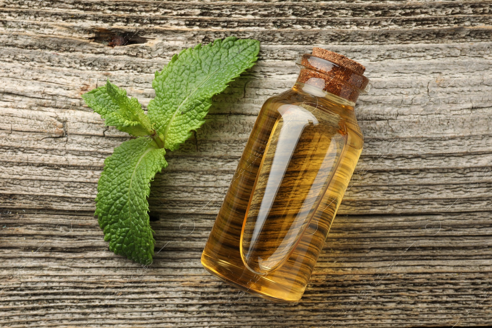 Photo of Bottle of mint essential oil and fresh leaves on wooden table, top view