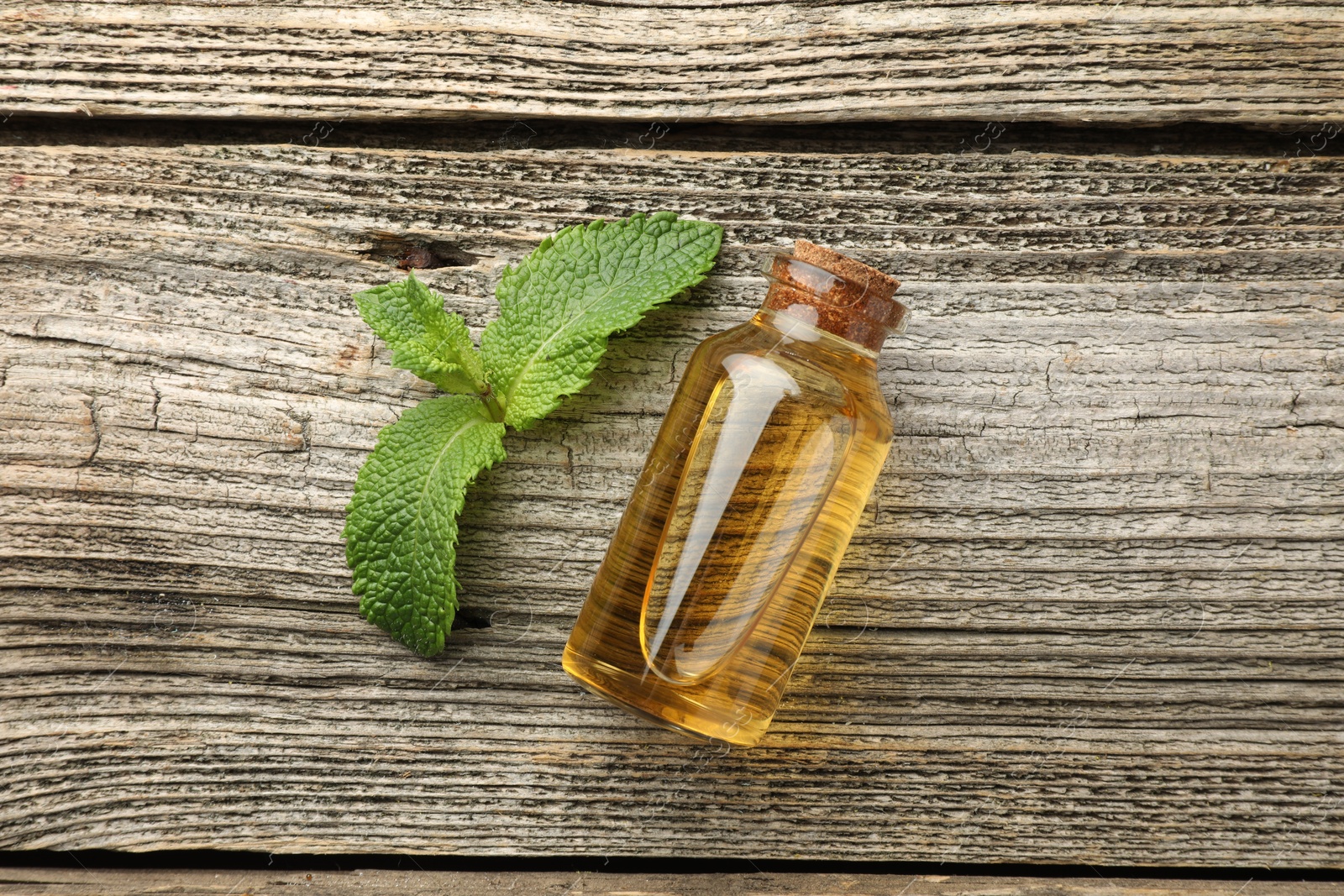 Photo of Bottle of mint essential oil and fresh leaves on wooden table, top view